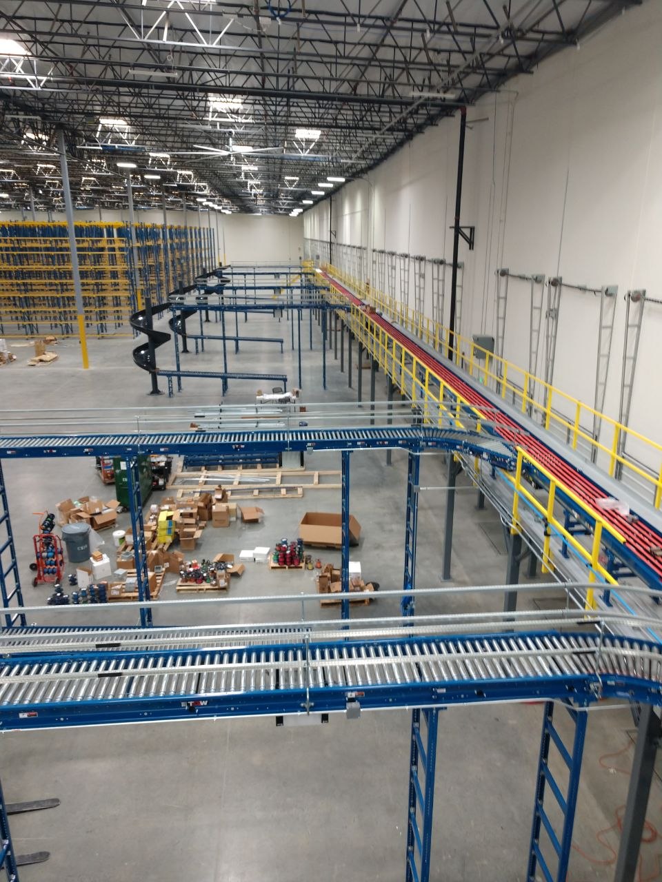 Large-scale conveyor system installation with blue roller conveyors, spiral chutes, and elevated walkways in a modern distribution facility